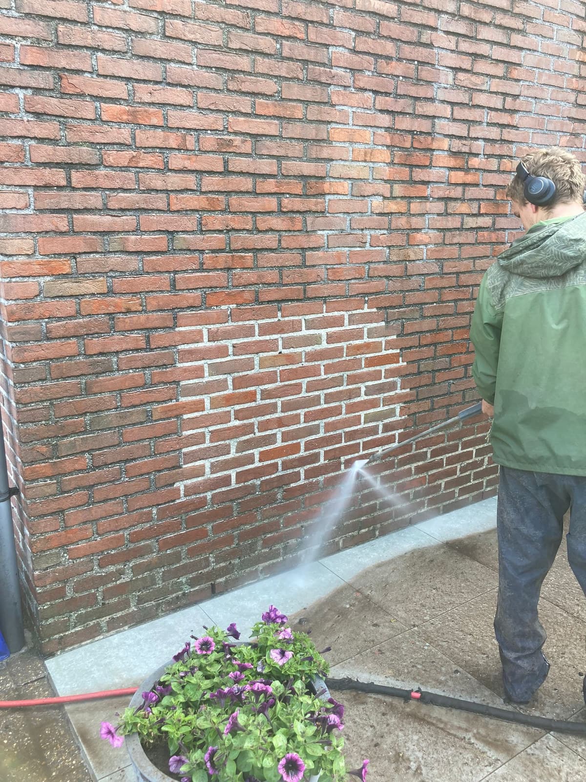 Vakman reinigt een bakstenen gevel, het proefvlak is duidelijk zichtbaar
