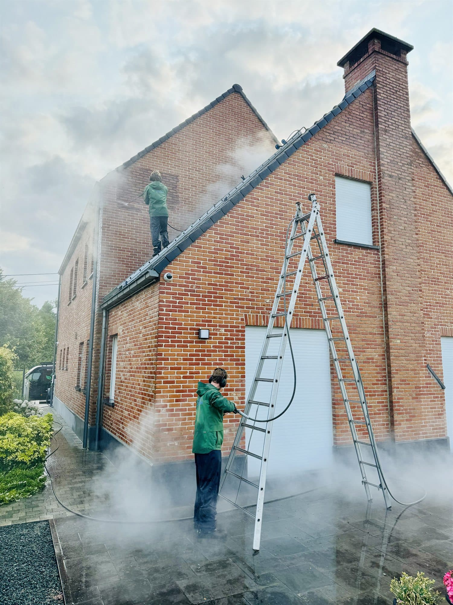 Medewerker reinigt een bakstenen puntgevel met duidelijk zichtbare stoom