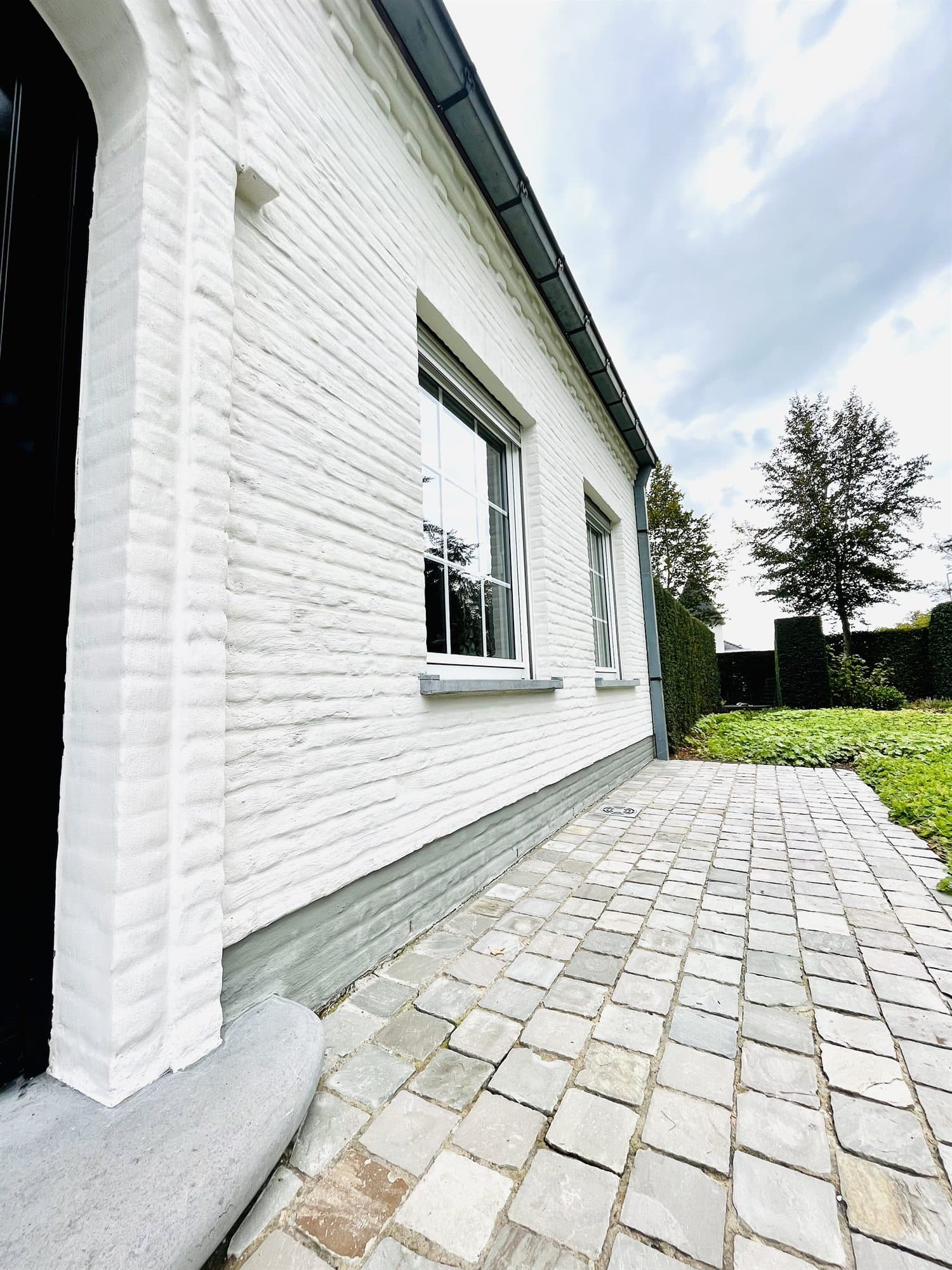 Zijgevel van een witte woning met gereinigde verharding ernaast