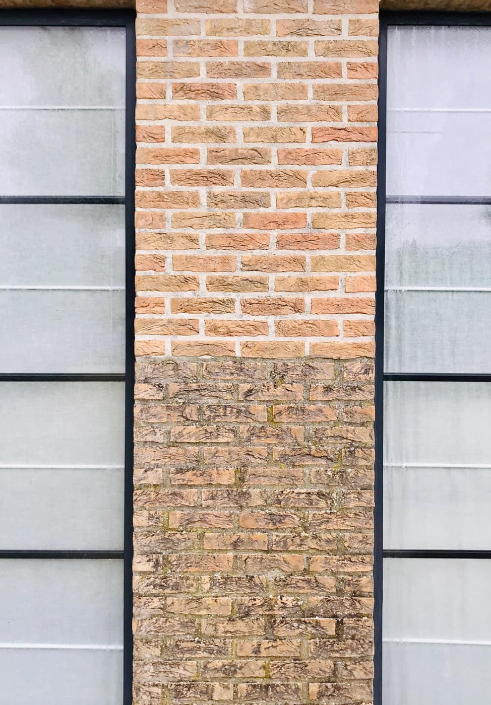 Bakstenen gevelpijler waarvan de bovenste helft gereinigd is en de onderste helft nog vervuild