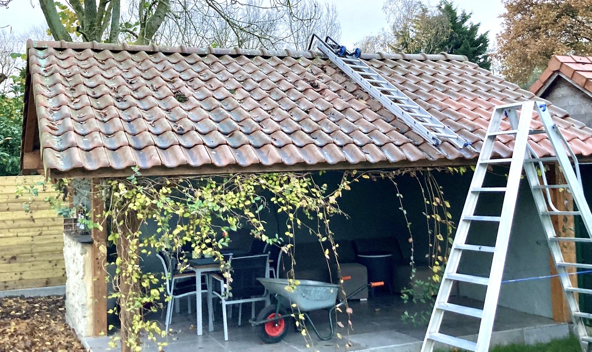 Carport met een bruin uitgeslagen pannendak, met de ladder nog tegen de dakrand